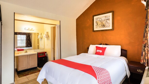 A hotel room with a bed, a nightstand, a bedside table, a small desk with a chair, a microwave, a sink, and a mirror. - OYO Hotel Decatur TX Hwy 287 Northwest (Decatur)