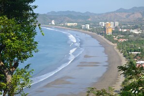 A coastal view with a beach, buildings, and greenery. - Casa Sunset - Ocean View House - Private Courtyard with Pool - Steps to Sand! (Jaco)