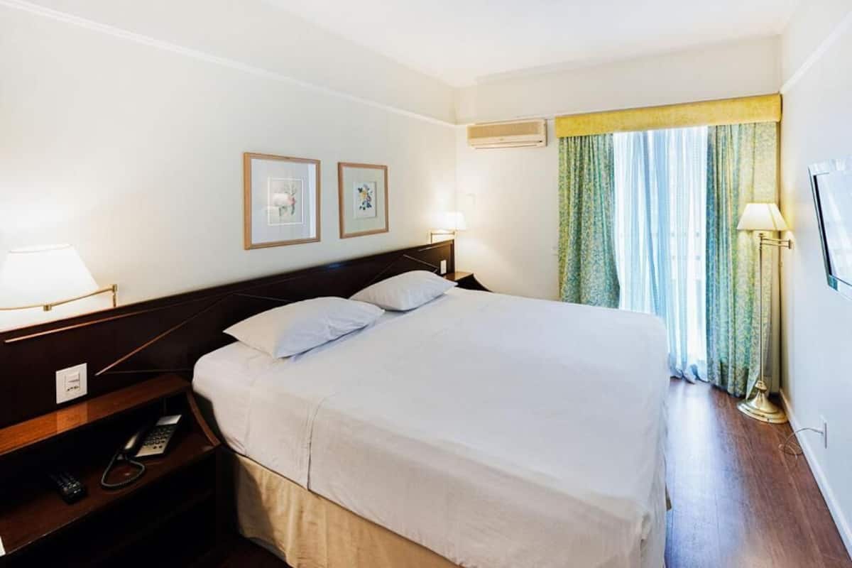 Une chambre d’hôtel avec un grand lit, des lampes de chevet, un téléphone et des tableaux encadrés au mur.