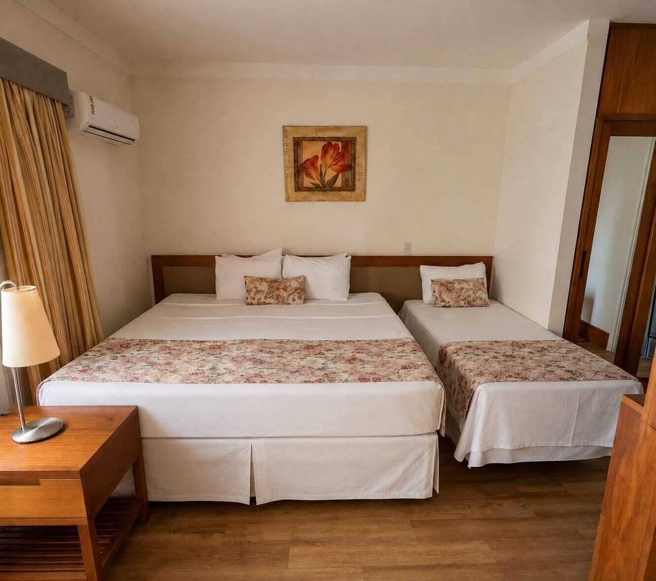 Una habitación de hotel con dos camas, una mesita de noche con lámpara, un escritorio de madera y un aire acondicionado instalado en la pared.