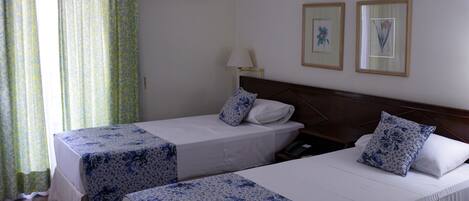 Una camera d'albergo con due letti, un comodino, una lampada e una finestra con tende.