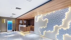Un área de recepción moderna con un mostrador de madera, un quiosco informativo digital y un diseño geométrico en la pared.