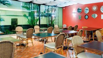 A restaurant with wicker furniture, red walls, and a view of greenery through large windows.