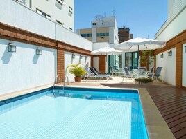 Una piscina al aire libre, sombrillas, sillones reclinables de piscina