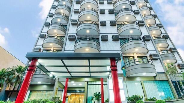 Un hotel de gran altura con varios balcones, una entrada de cristal y pilares rojos.