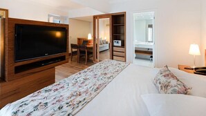 Habitación de hotel con una televisión de pantalla grande, una cama con ropa de cama floral, un escritorio con una silla y un armario.