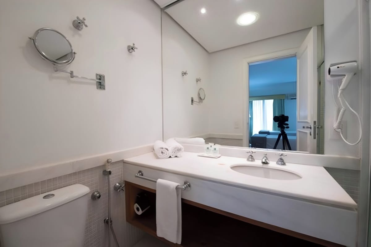 A modern bathroom with a large mirror, two sinks, a towel rack, and a shower.