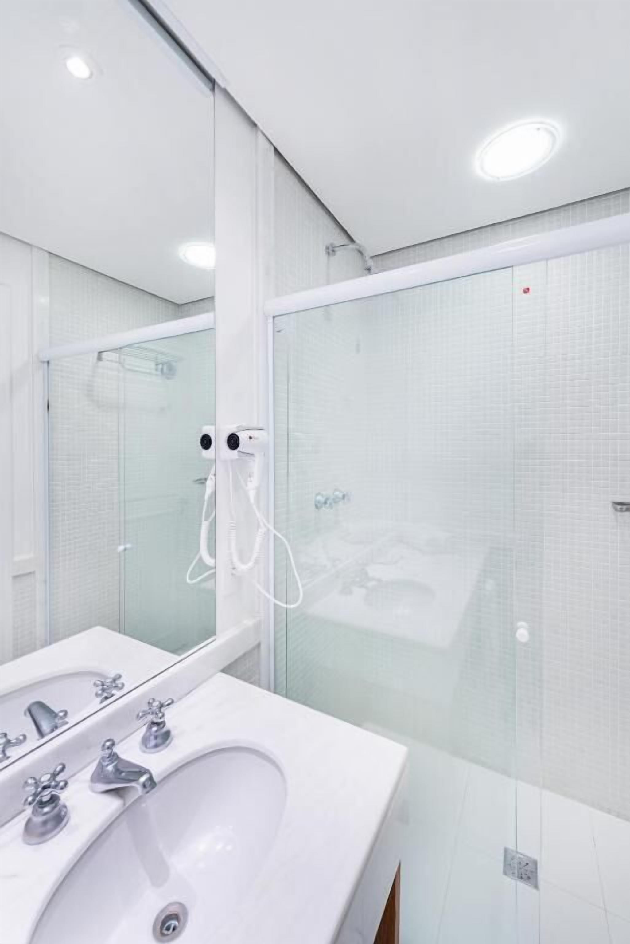Un baño moderno con cabina de ducha de vidrio, un lavamanos blanco con múltiples grifos y un espejo grande.