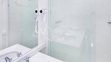 Un baño moderno con cabina de ducha de vidrio, un lavamanos blanco con múltiples grifos y un espejo grande.