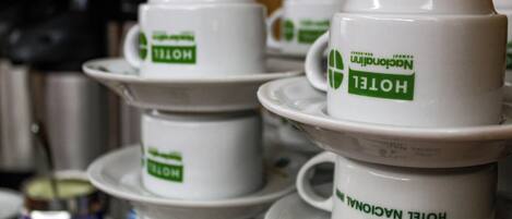 Une pile de tasses blanches provenant d’un hôtel, ornées de logos verts, disposées sur une table.