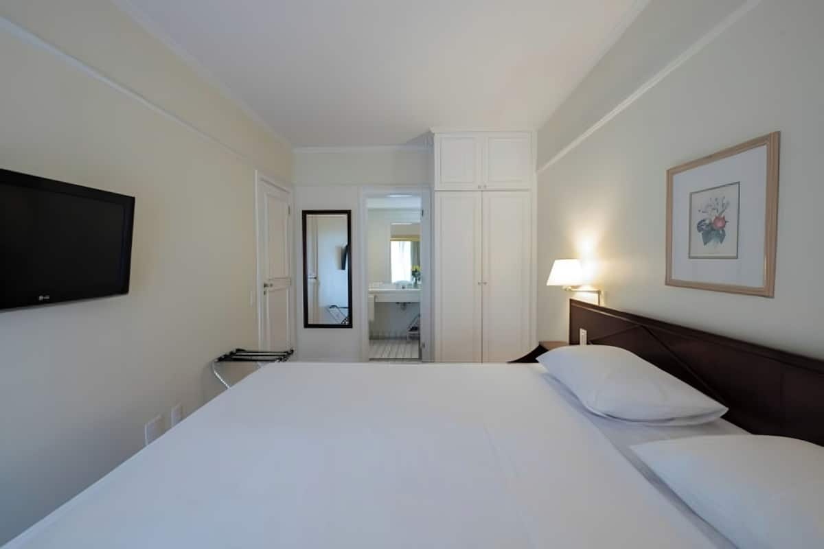 Une chambre d’hôtel avec un grand lit, un téléviseur fixé au mur, une lampe de chevet et un tableau encadré.
