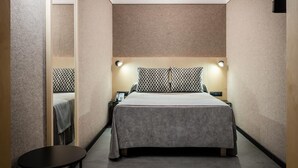 Hotellihuone, jossa on sänky, yöpöydät, pieni pöytä ja seinään kiinnitetty valaisin.
