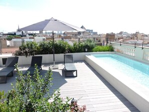 A rooftop pool area with lounge chairs and a large umbrella, surrounded by greenery and overlooking a cityscape. - Raval House (Barcelona)