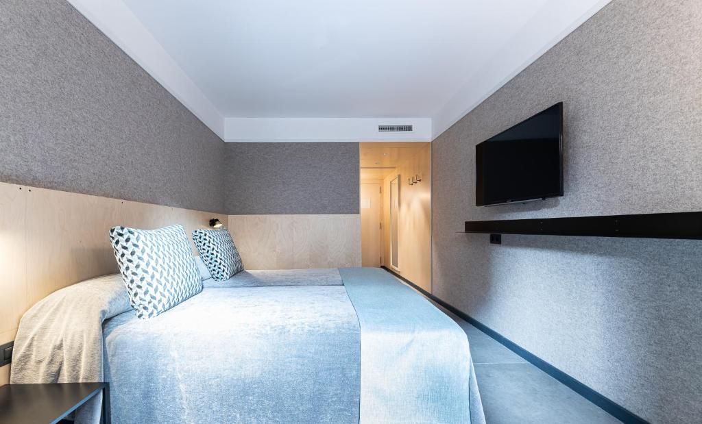 Una habitación de hotel moderna con una cama grande, un televisor de pantalla plana montado en la pared y una puerta de madera que da al baño.
