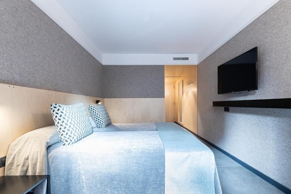 Una habitación de hotel moderna con una cama grande, un televisor de pantalla plana montado en la pared y una puerta de madera que da al baño.