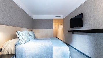 Una habitación de hotel moderna con una cama grande, un televisor de pantalla plana montado en la pared y una puerta de madera que da al baño.