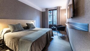 Habitación de hotel con dos camas, un escritorio, una silla, un televisor y una ventana con cortinas.