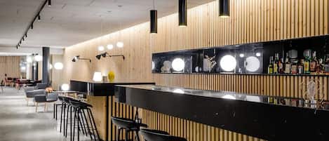 Un espace bar moderne avec un mur lambrissé en bois, un comptoir de bar noir et des tabourets de bar noirs.