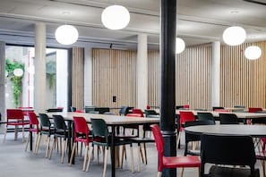 Un comedor moderno con varias mesas y sillas, con una combinación de mesas redondas y rectangulares, y una variedad de colores de sillas.