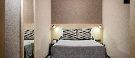 A hotel room with a bed, bedside tables, a small table, and a wall-mounted light fixture.