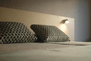 Una cama con almohadas estampadas y una lámpara fijada a la pared.
