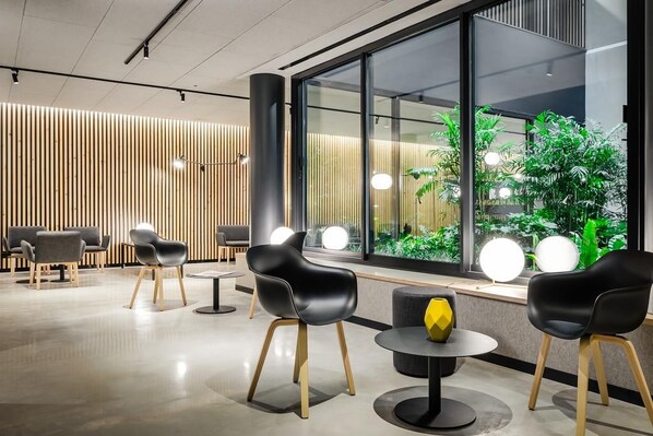 A modern interior with a seating area, a large window with a view of greenery, and a decorative yellow object on a table. - Raval House (Barcelona)