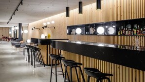 Un área de bar moderna con una encimera negra, paneles de madera y taburetes negros.