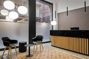 Una moderna zona de recepción con un mostrador negro, dos sillas negras, una pequeña mesa redonda y un suelo con diseño.