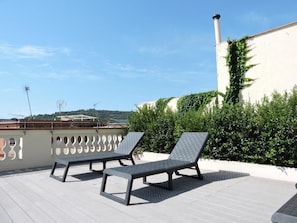 A rooftop terrace with two sun loungers and a table, surrounded by greenery and a white building with a chimney. - Raval House (Barcelona)