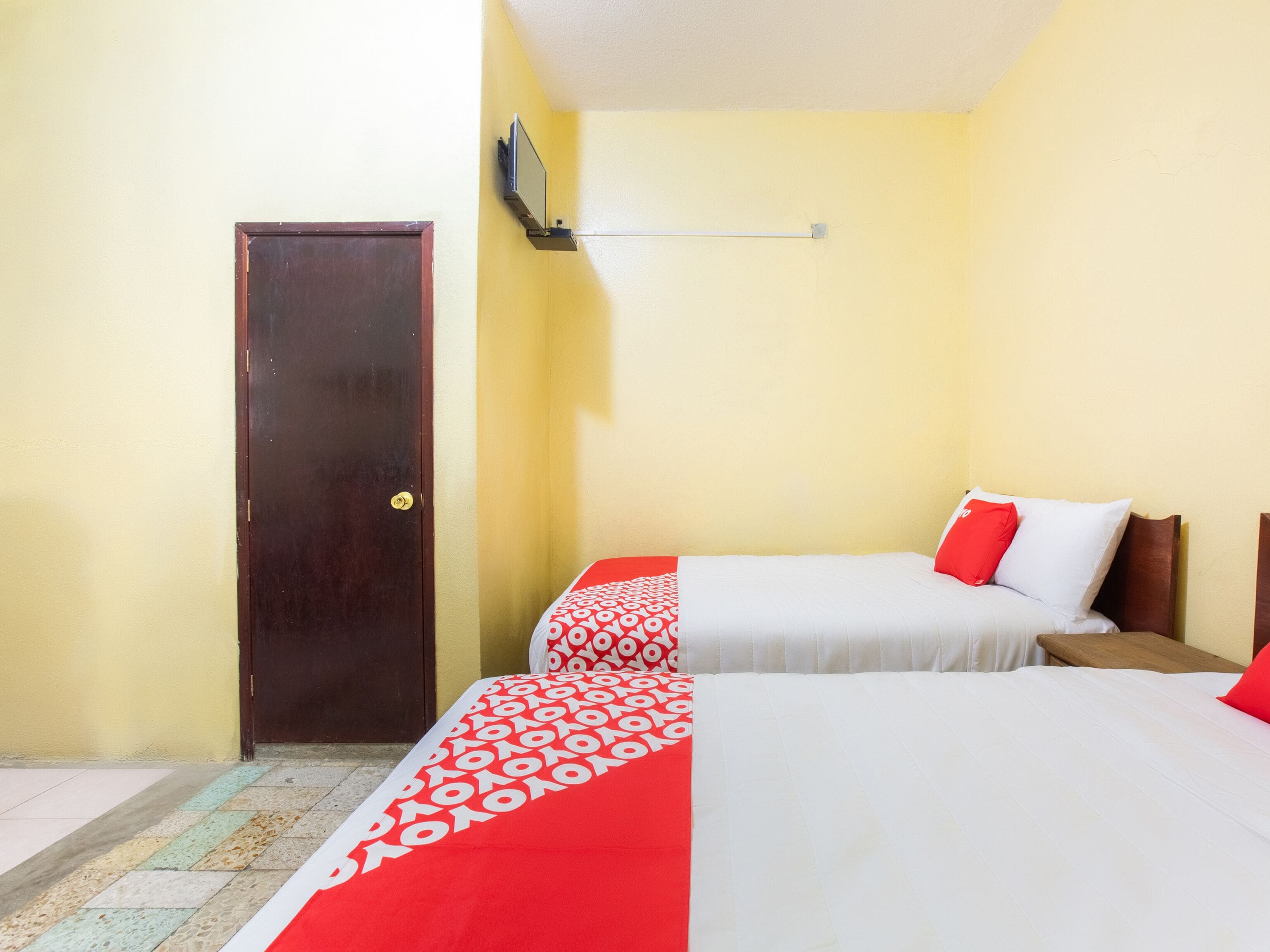 Una habitación con dos camas, una puerta de madera y una lámpara fijada a la pared.