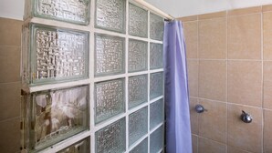 Ducha con cabezal de ducha de lluvia, puerta de vidrio con diseño geométrico y pared revestida de azulejos.