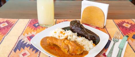 A plate of food with rice, a meat dish, and a glass of a yellowish beverage on a table with a colorful tablecloth.