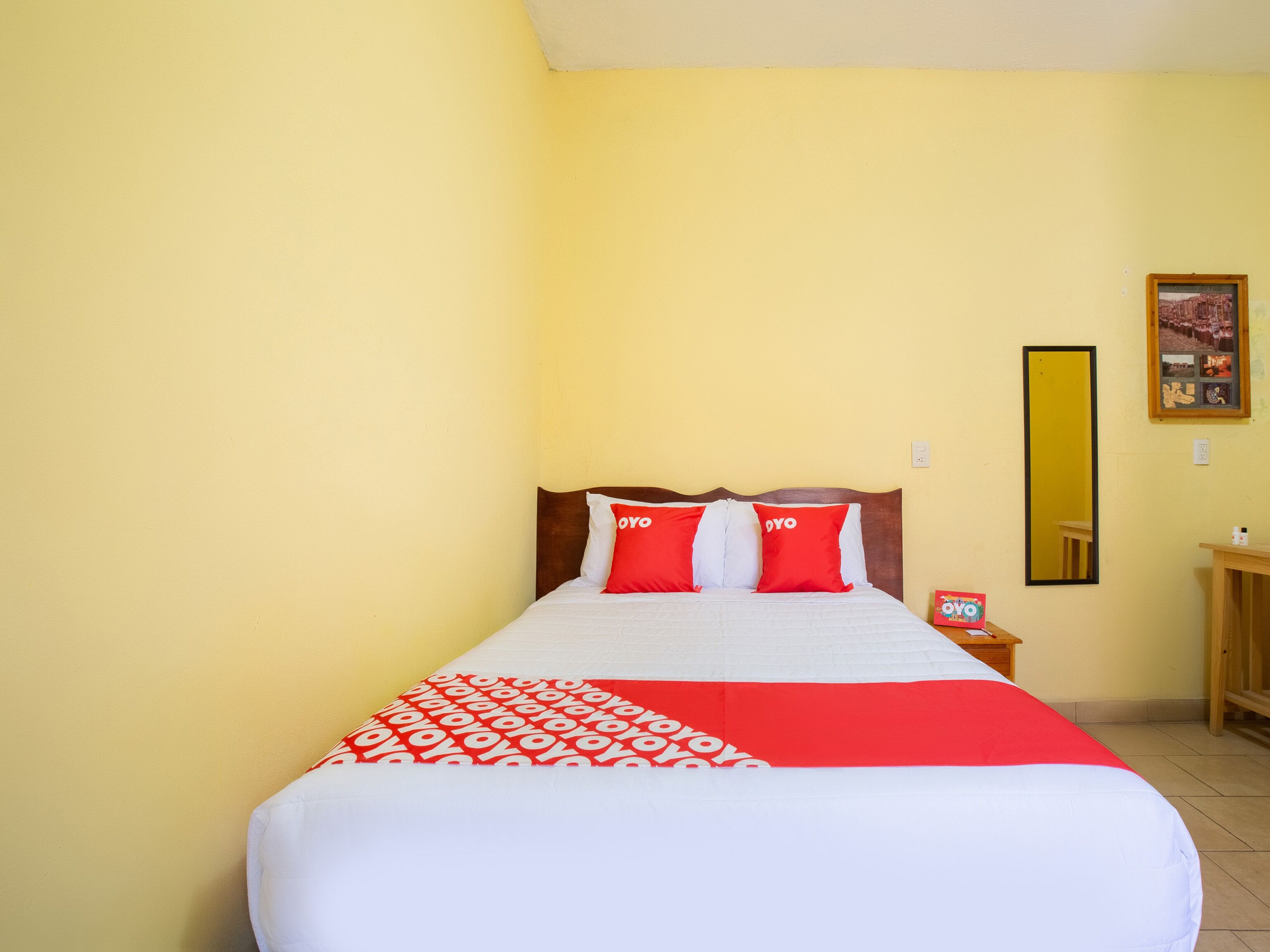 A bed with a white and red bedspread, two red pillows with 'YOYO' text, a wooden headboard, and a nightstand with a small lamp.