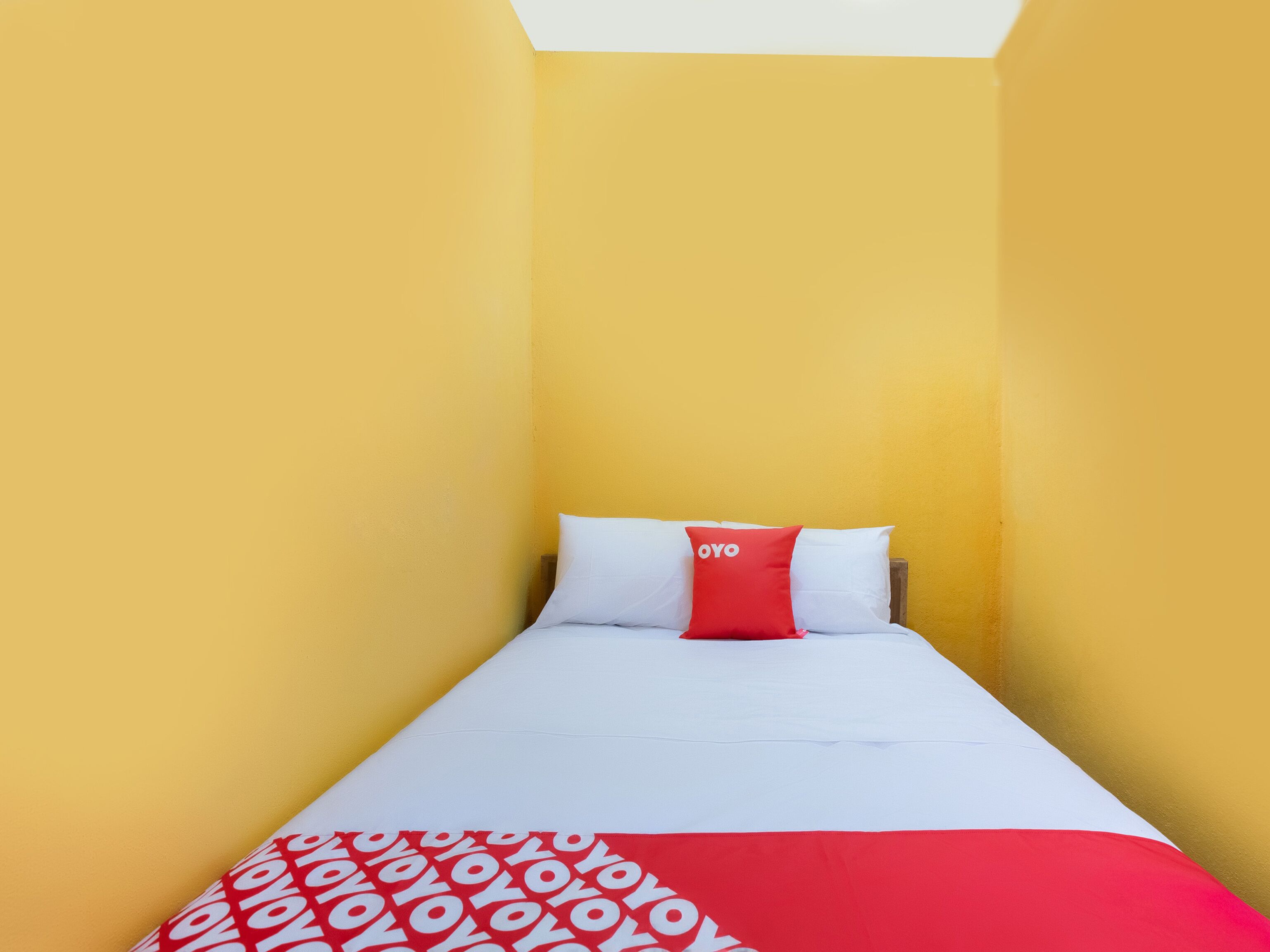 Een eenpersoonsbed met wit en rood beddengoed, een rood kussen met de tekst 'YOYO' erop, en een deken met een rood-wit patroon.