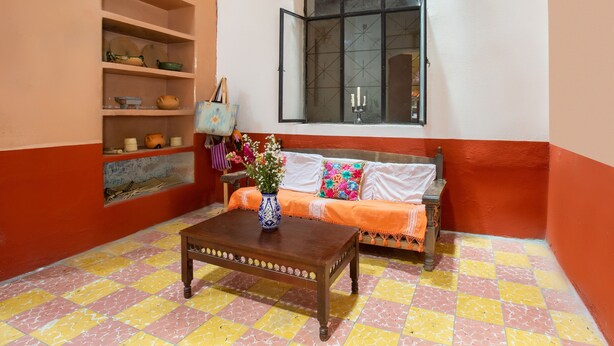 Una sala de estar acogedora con una mesa de centro de madera, un sofá con una manta naranja y una ventana con marco negro.