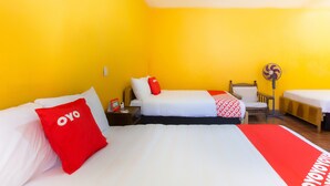 Una habitación de hotel con dos camas, una mesita de noche, una silla y un ventilador de pie.