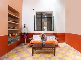 Una habitación con un banco de madera, una mesa con un florero, estanterías con cerámica y una ventana con vistas.
