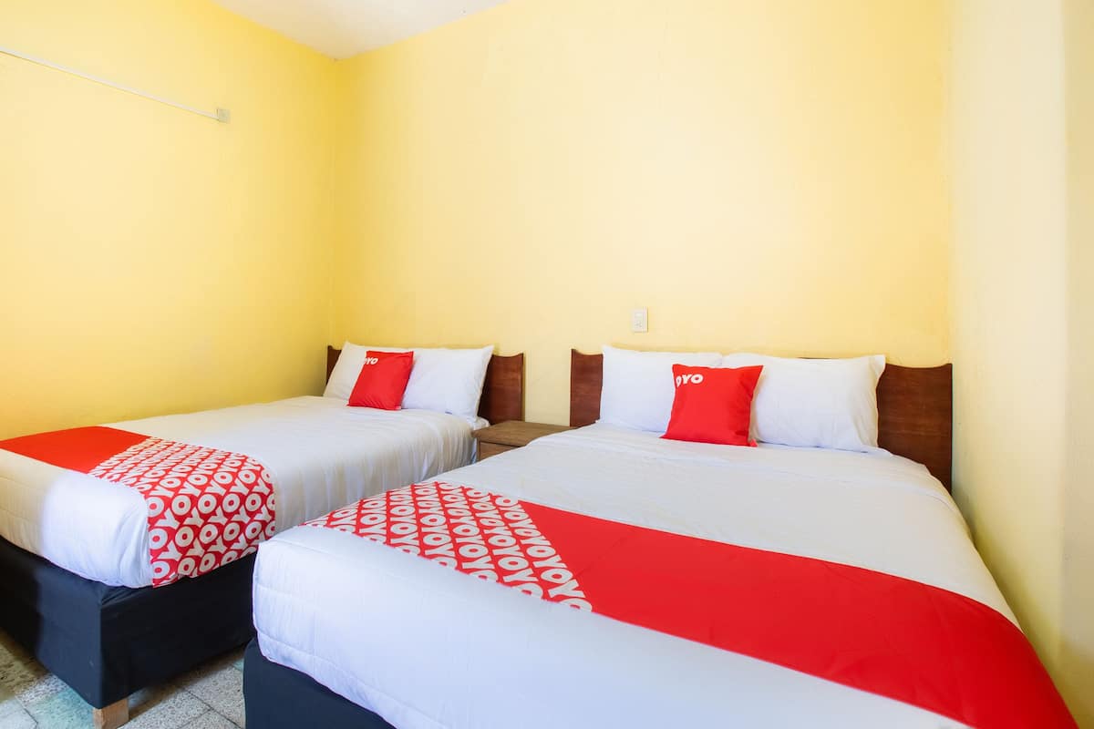 A hotel room with two beds, each with a red and white patterned bedspread and pillows, and a wooden headboard.