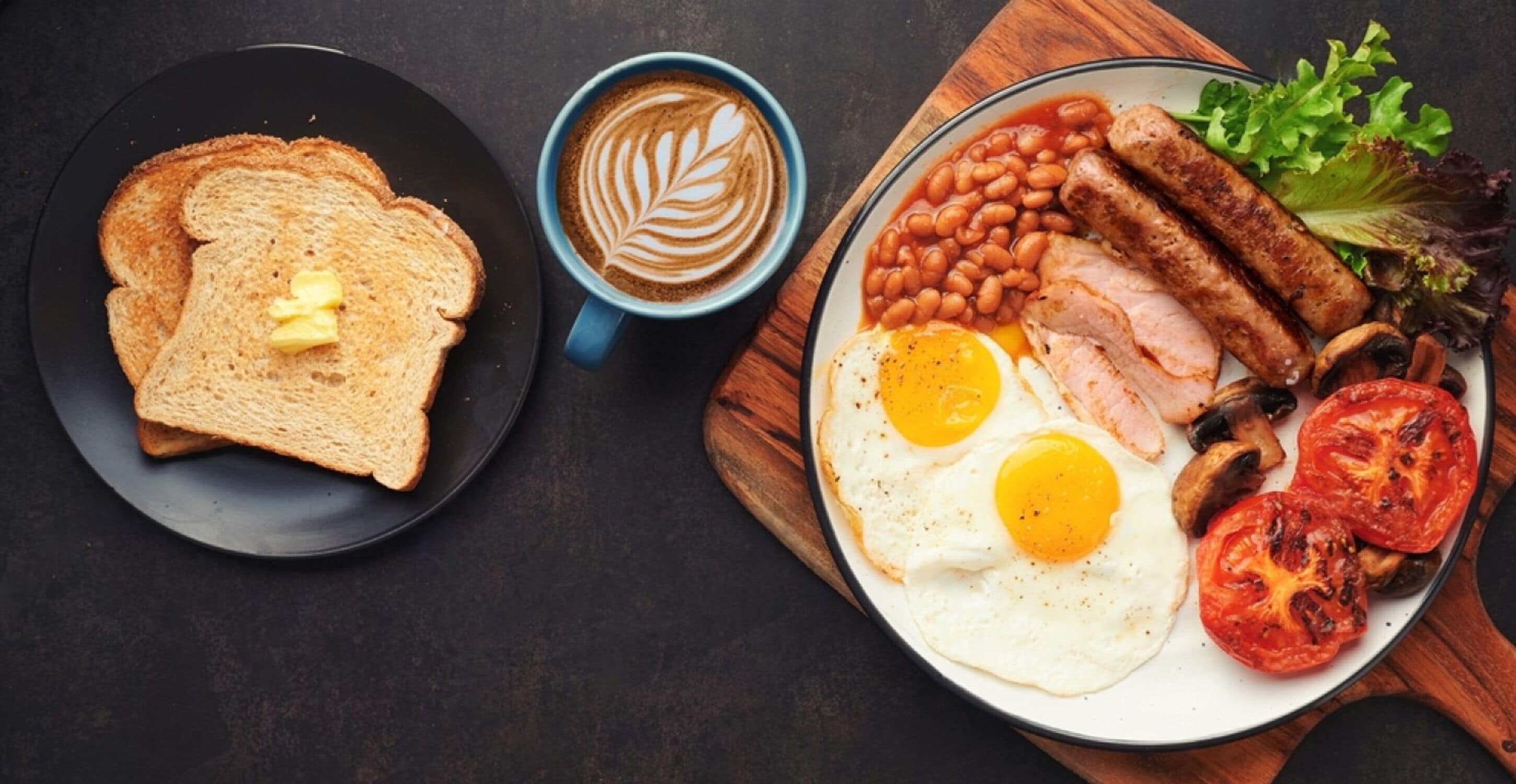 Une assiette de petit-déjeuner comprenant des toasts, des œufs, des saucisses, des haricots, des tomates et une tasse de café.
