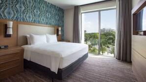 Habitación de hotel con una cama grande, una mesita de noche, un televisor y un ventanal con vista a la ciudad.