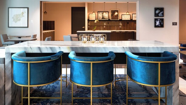 Un comedor moderno con una mesa de mármol, tres sillas de terciopelo azul con detalles dorados y una alfombra estampada.