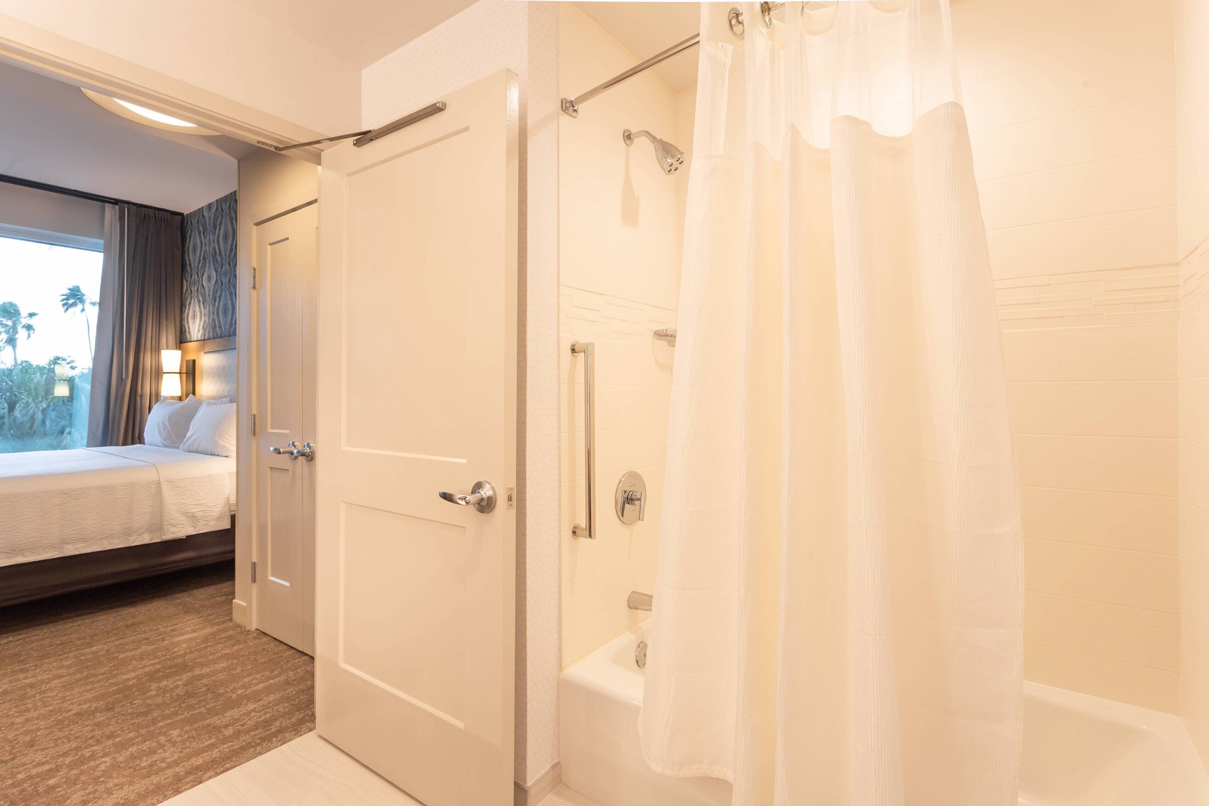 Una habitación de hotel con cama, ducha y ventana con cortinas.