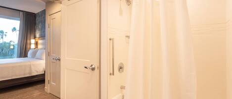 Una habitación de hotel con cama, ducha y ventana con cortinas.