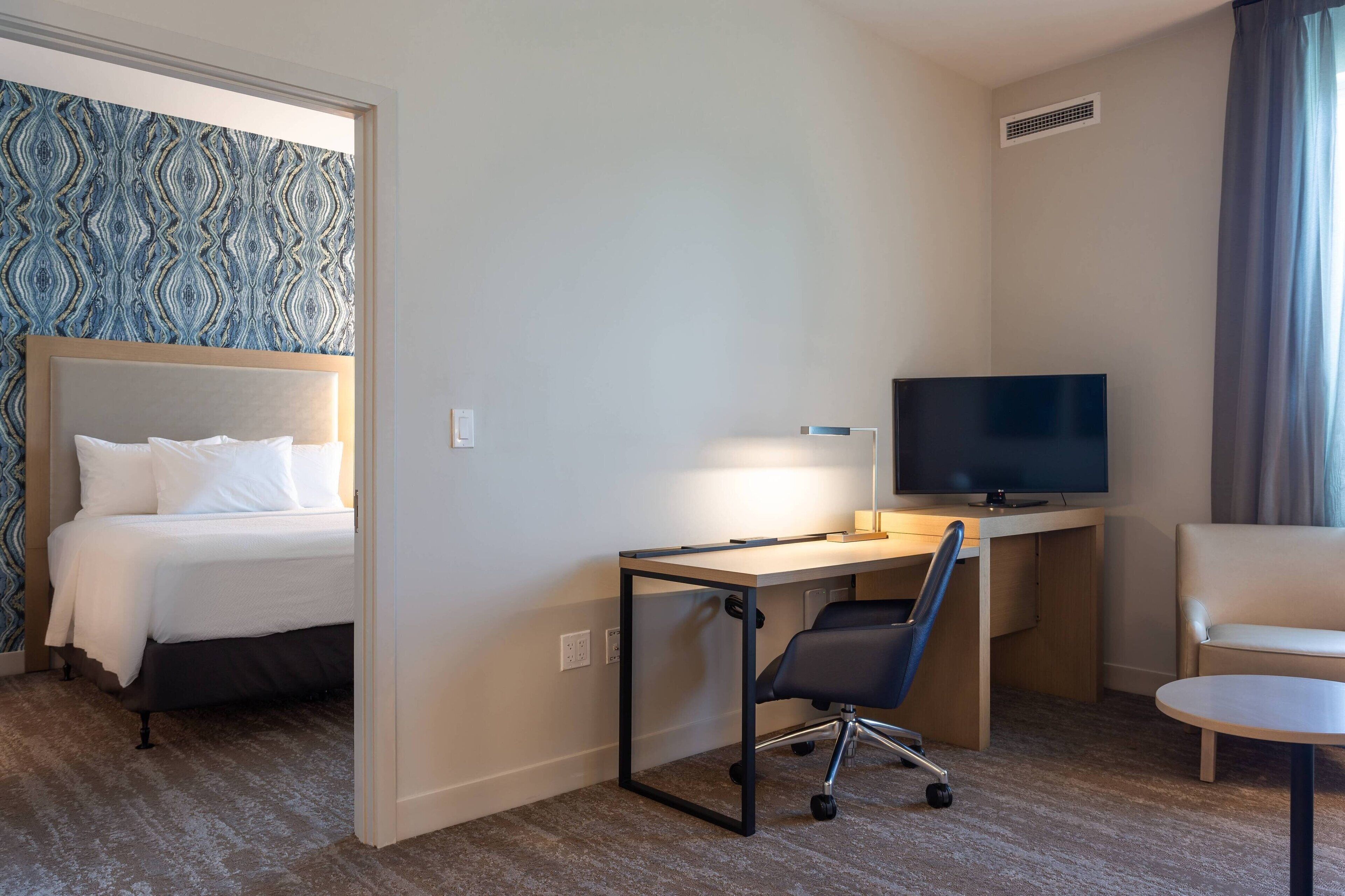 A hotel room with a bed, a desk with a computer, a TV, and a chair.