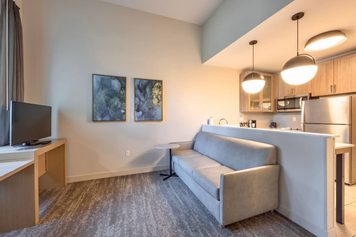 A modern kitchen with a built-in microwave and refrigerator, a gray sofa, and a small table.