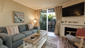 Ein Wohnzimmer mit Sofa, Couchtisch, Fernseher, Kamin und Blick durch die Glastür.