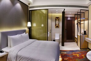 Une chambre d’hôtel avec un grand lit, une salle de bain avec des toilettes et un lavabo, et un espace douche.