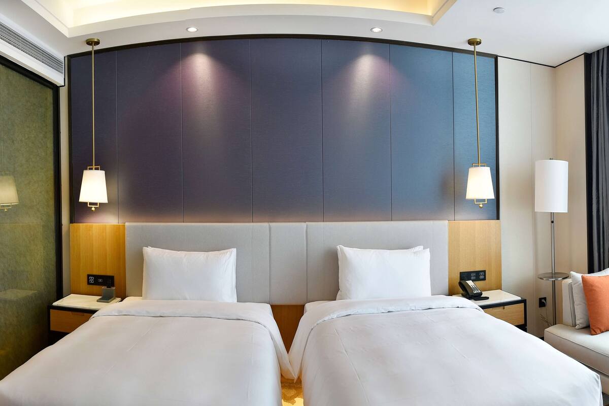 Une chambre d’hôtel avec deux lits, une grande tête de lit, des lampes de chevet, une table de chevet avec un téléphone et un canapé avec un coussin.