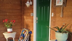 A wooden exterior with a green door, a white wicker table with a potted plant, and a blue cooler on a white stand.
