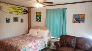 A bedroom with a bed, a chair, a ceiling fan, and artwork on the walls.